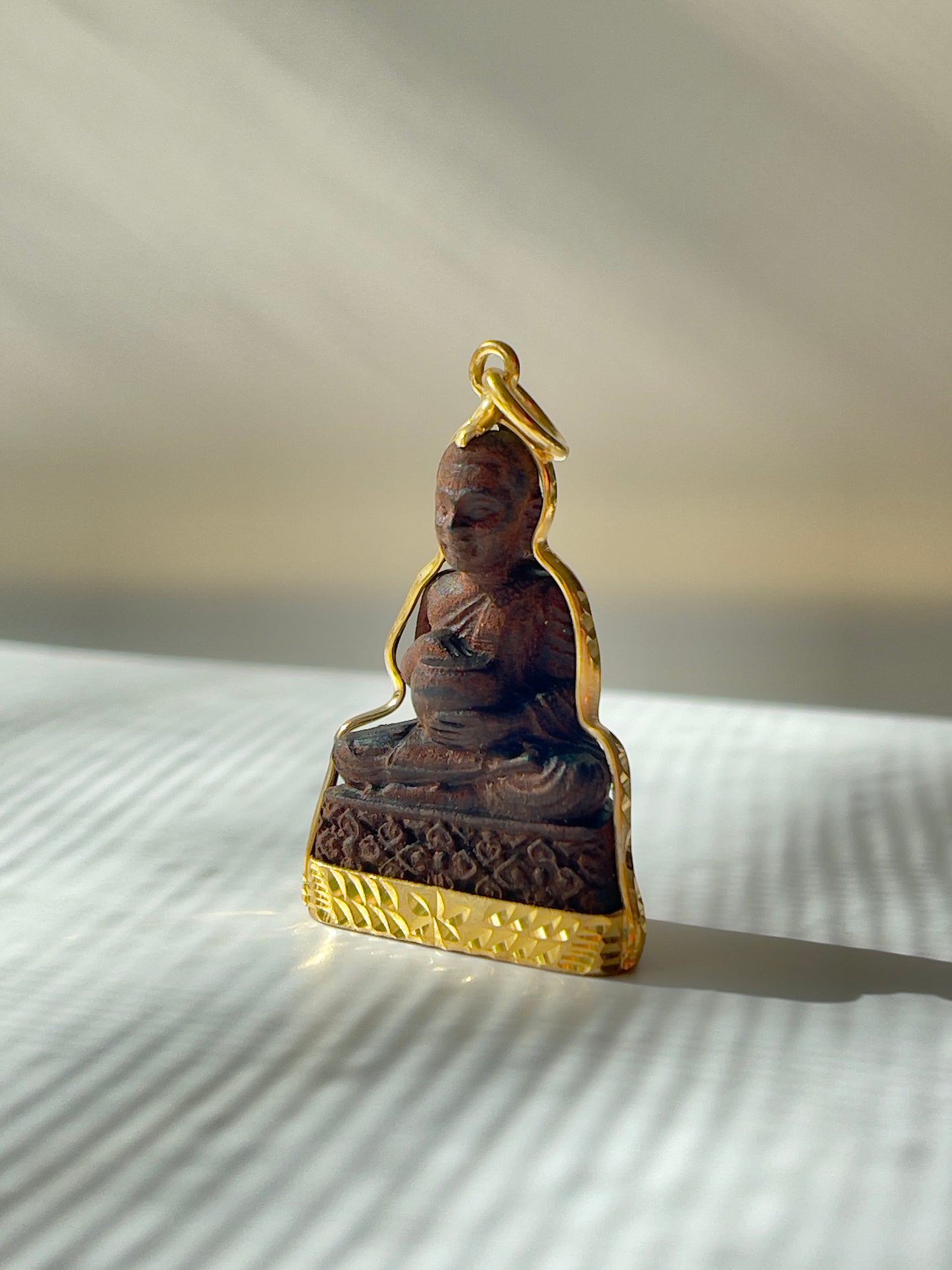 Angled view of Wooden Khmer style Buddha in a gold plated mounting. 